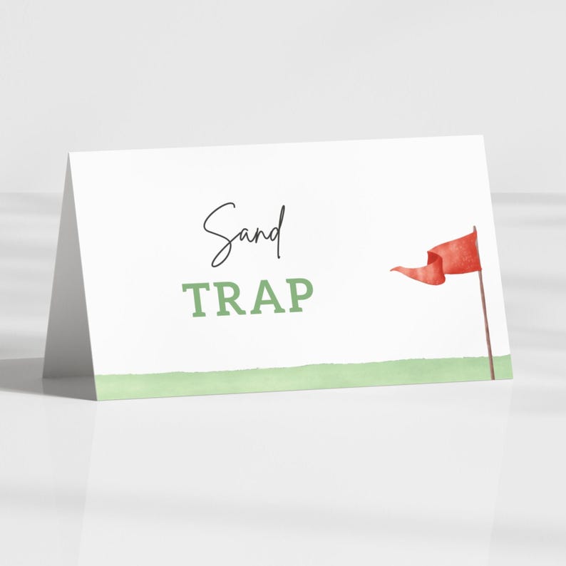 May include: A white folded card with the words "Sand TRAP" in black and green. A red flag on a brown pole is on the right side of the card. A green watercolor-style line is at the bottom of the card.