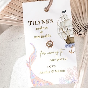 Puede incluir: Una etiqueta de agradecimiento blanca con letras doradas. La etiqueta presenta una cola de sirena, un barco pirata y un ancla náutica. El texto dice "THANKS mateys & mermaids for coming to our party! LOVE Amelia & Mason".