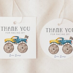 May include: Two thank you tags with a monster truck design. The tags are white with black text that says "Thank You for Racing By!" and "Love, Incas". The monster truck is blue, yellow, and gray with flames on the side.