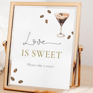 Op de afbeelding: Een gouden lijst met de tekst "Love is Sweet" en een aquarel-illustratie van een koffie drankje met koffiebonen. Het bord zegt ook "Please take a treat!"