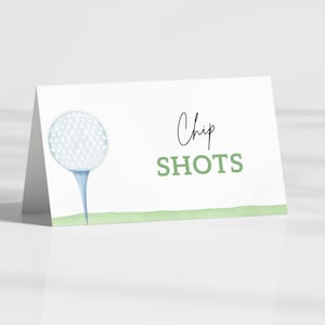 May include: A white folded card featuring a golf ball on a tee illustration. The text "Chip SHOTS" is in green and black script. A green watercolor line is at the bottom of the card.