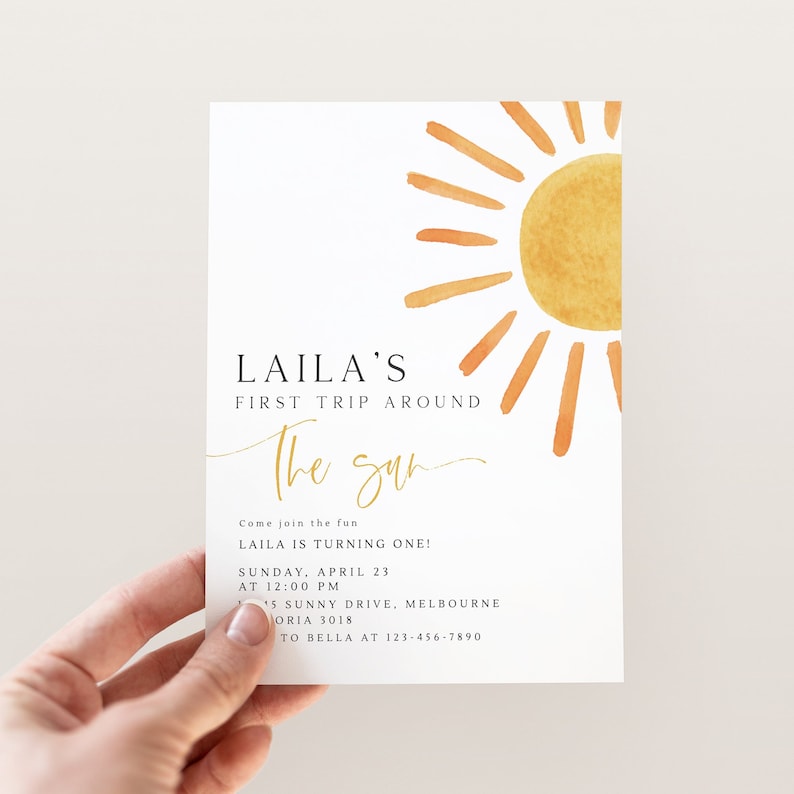 Peut inclure: Une illustration aquarelle d'un soleil dans des tons jaunes et orange. Le texte "LAILA'S FIRST TRIP AROUND The sun" est &eacute;crit en lettres noires et dor&eacute;es. Le texte ci-dessous indique "Come join the fun LAILA IS TURNING ONE! SUNDAY, APRIL 23 AT 12:00 PM 15 SUNNY DRIVE, MELBOURNE VICTORIA 3018 TO BELLA AT 123-456-7890".