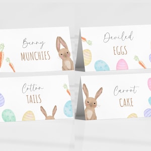 May include: Four white printable food labels with bunny illustrations and Easter-themed food names. The labels read "Bunny Munchies", "Cotton Tails", "Carrot Cake", and "Deviled Eggs".