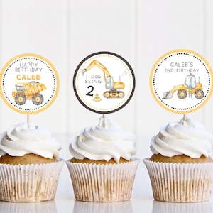 May include: Three yellow and black cupcake toppers with construction vehicle designs. The toppers say "Happy Birthday Caleb", "I Dig Being 2", and "Caleb's 2nd Birthday".