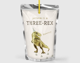May include: A silver juice pouch with a yellow straw. The pouch has a white label with a cartoon illustration of a green dinosaur wearing a party hat. The text on the label reads "Jayden is a THREE-REX Rawrr!!"