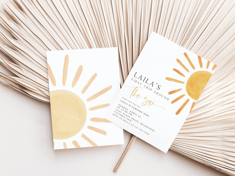 Peut inclure: Une carte d'invitation blanche avec un graphique de soleil jaune et le texte "LAILA'S FIRST TRIP AROUND THE SUN" et des d&eacute;tails pour une f&ecirc;te de premier anniversaire.