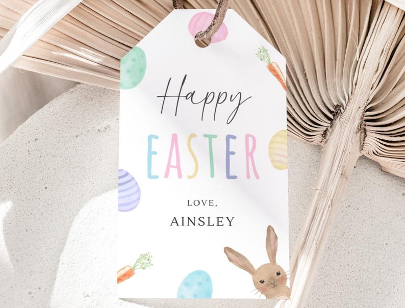 May include: White gift tag with a watercolor illustration of Easter eggs, carrots, and a bunny. The text reads "Happy Easter" in colorful letters and "Love, Ainsley".