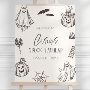 K&ouml;nnte beinhalten: Ein wei&szlig;es Willkommens-Schild mit schwarzen Illustrationen von Geistern, K&uuml;rbissen, Flederm&auml;usen, S&uuml;&szlig;igkeiten und einem Spinnennetz. Der Text lautet "Willkommen zu Caseys Spook-Tacular Second Birthday".