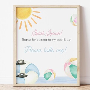May include: A framed watercolor print with a light wood frame. The print features a yellow sun, beach balls, and a pool float. Text reads "Splish Splash! Thanks for coming to my pool bash. Please take one!"