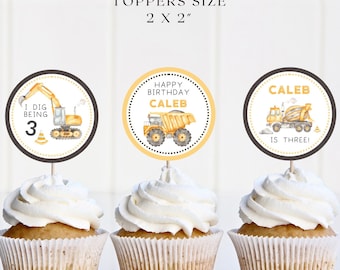 May include: Three construction vehicle themed cupcake toppers. The toppers are 2 inches by 2 inches. One topper says "I dig being 3" with a yellow excavator. Another topper says "Happy Birthday Caleb" with a yellow dump truck. The third topper says "Caleb is three!" with a yellow cement mixer.