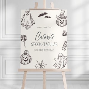K&ouml;nnte beinhalten: Ein wei&szlig;es Willkommens-Schild mit schwarzen Illustrationen von Geistern, K&uuml;rbissen, Flederm&auml;usen, S&uuml;&szlig;igkeiten und einem Spinnennetz. Das Schild lautet "Willkommen zu Caseys Spook-tacular Second Birthday".