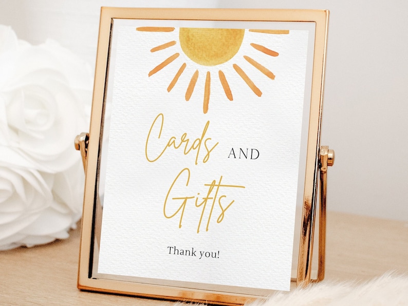 May include: A gold framed sign with a watercolour sun illustration and the text "Cards and Gifts" with the words "Thank you!" at the bottom.