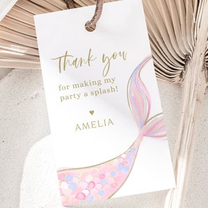 May include: Thank you for making my party a splash! Amelia. A white thank you tag with gold text and a pink and blue mermaid tail illustration.