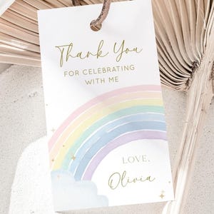 May include: A white thank you tag with a rainbow and gold stars. The text reads "Thank You for celebrating with me. Love, Olivia."