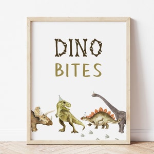 May include: A white printable sign with the text "Dino Bites" in brown and gold lettering. The sign features a cartoon illustration of four dinosaurs wearing party hats.