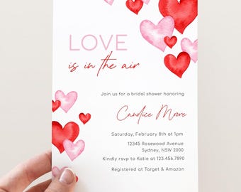 Puede incluir: Una invitación a una despedida de soltera con un diseño de corazones de acuarela rosa y rojo. El texto dice "LOVE is in the air" e incluye detalles del evento, como la fecha, la hora, la ubicación y la información de RSVP. La invitación también menciona que la novia está registrada en Target y Amazon.