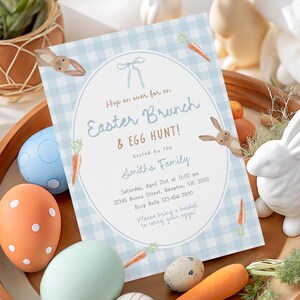 May include: An Easter Brunch & Egg Hunt invitation with a blue gingham background, bunny and carrot illustrations. The invitation is surrounded by decorative Easter eggs, a white ceramic bunny, and a wooden tray.