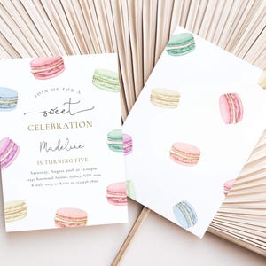 May include: A white invitation card with a gold border and text that reads "Join us for a sweet celebration Madeline is turning five". The card is decorated with watercolor illustrations of colorful macarons.