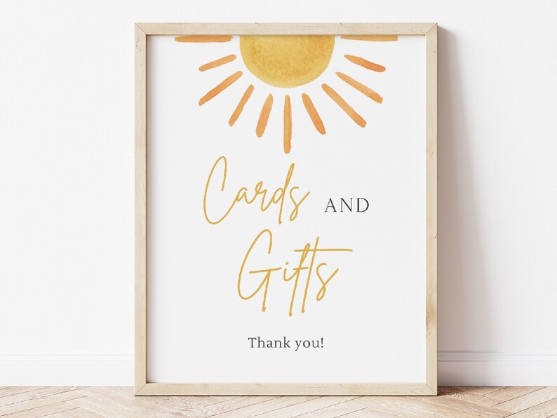 May include: A white sign with a yellow sun graphic and the text "Cards and Gifts" in gold script. The sign also includes the text "Thank you!" in black.