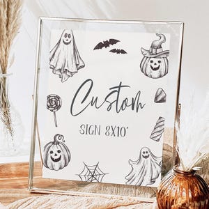 May include: A white sign with black Halloween-themed illustrations, including ghosts, pumpkins, bats, and candy. The sign reads "Custom Sign 8x10".