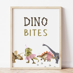 May include: A printable sign with the text "Dino Bites" in brown and gold letters. The sign features a watercolor illustration of four dinosaurs, including a green T-Rex wearing a pink tutu and a party hat.