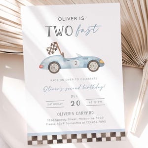 Puede incluir: Una invitación de cumpleaños azul claro con una ilustración de acuarela de un coche de carreras vintage. El texto dice "Oliver tiene dos años" e incluye detalles del evento. Una bandera a cuadros ondea desde el coche.