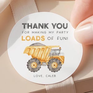 May include: A round sticker with the text "THANK YOU FOR MAKING MY PARTY LOADS OF FUN!" and a watercolor illustration of a yellow dump truck. The sticker is being held by a hand.