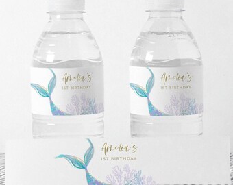 Op de afbeelding: Waterfleslabels met een zeemeerminstaart en koraalontwerp. De labels zijn wit met gouden tekst die "Amelia's 1st Birthday" zegt.