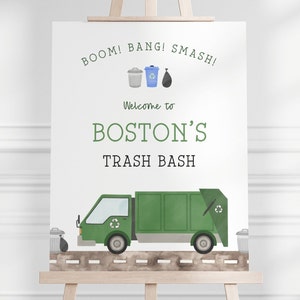 May include: A green garbage truck with a recycling symbol on the side. The truck is driving on a brown road with two green trash cans on either side. The sign above the truck says "BOOM! BANG! SMASH! Welcome to BOSTON'S TRASH BASH".