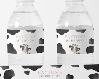 May include: Water bottle labels with a cow print background and the text "PAYTON'S 1ST BIRTHDAY" in pink. A cartoon cow with a pink flower crown is in the center of the label.