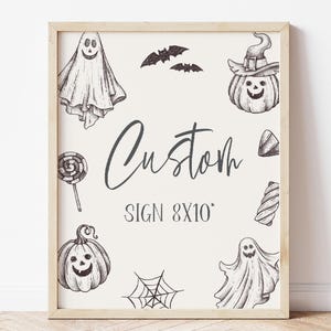 May include: A white sign with a black frame, featuring a custom sign design with the text "Custom Sign 8x10" and various Halloween-themed illustrations, including ghosts, pumpkins, bats, and candy.