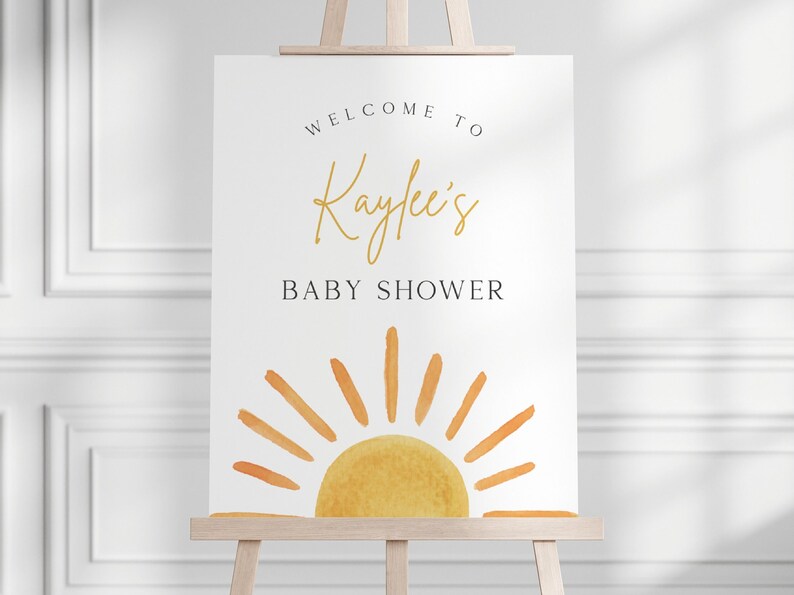 May include: Welcome to Kaylee's Baby Shower sign with a watercolor illustration of a yellow sun with orange rays on a white background.