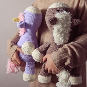 Peut inclure: Deux animaux en peluche faits à la main au crochet. L'un est une licorne violette avec une corne jaune et une crinière et une queue roses. L'autre est un mouton marron et blanc avec une barbe et une queue blanches et duveteuses.