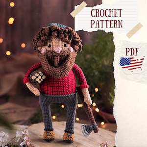 Puede incluir: Patrón de crochet PDF para un amigurumi de leñador. La muñeca lleva una camisa de cuadros rojos y negros, pantalones vaqueros azules y una barba marrón. Lleva un manojo de troncos en una mano y un hacha en la otra.