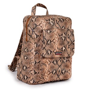 Può includere: Zaino con motivo a pelle di serpente nei toni del marrone, beige e nero. Presenta una tasca frontale, un manico superiore e spallacci regolabili. La cerniera e le finiture sono marroni. Il marchio "SKINTAN" è visibile sulla tasca anteriore.