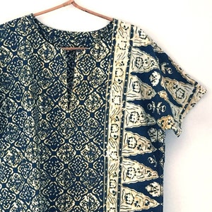 May include: A blue and gold patterned tunic with a short sleeve and a V-neck. The tunic has a decorative border on the right side.