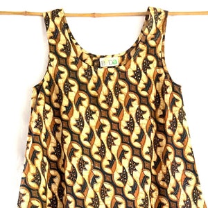 May include: A sleeveless dress with a brown and yellow batik pattern. The dress has a scoop neck and a loose fit.