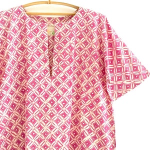 May include: A pink and white patterned short-sleeved shirt with a keyhole neckline.