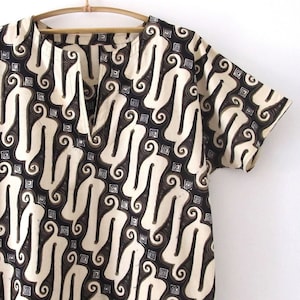 May include: A short-sleeved shirt with a brown and white batik pattern. The shirt has a V-neck and is made of a lightweight fabric.