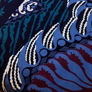 May include: Close-up of a fabric with a batik design. The fabric features a dark blue background with patterns in white, teal, and shades of blue and burgundy. The design includes stylized floral and geometric shapes.