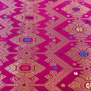May include: A close-up of a pink fabric with a gold woven pattern. The pattern features intricate geometric shapes and small colorful flowers.