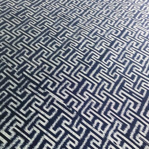 May include: Close-up of a textile with a repeating geometric pattern. The design features a series of interconnected, white, maze-like shapes against a dark blue background. The fabric has a slightly textured appearance.
