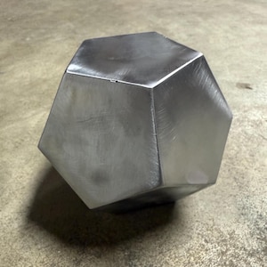 Puede incluir: Una escultura geométrica de metal plateado con un diseño facetado. La escultura tiene un acabado liso y pulido y tiene forma de dodecaedro.