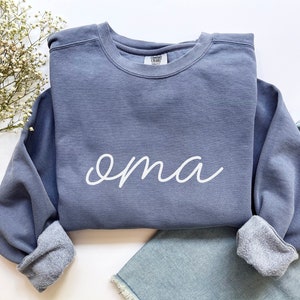 May include: A blue sweatshirt with the word "oma" written in white cursive on the front.