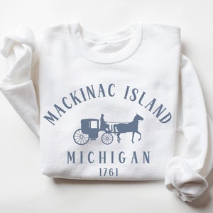 May include: White sweatshirt with a blue graphic of a horse-drawn carriage and the text "Mackinac Island Michigan 1761".