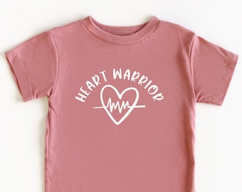 May include: A pink short-sleeved t-shirt with a white graphic of a heart with an EKG line and the text "HEART WARRIOR" around it.
