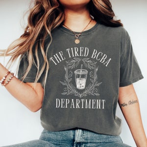 May include: A grey t-shirt with the text "The Tired BCBA Department" and a graphic of a cup of boba tea with a straw.