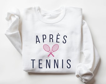 May include: White sweatshirt with the text "APRÈS TENNIS" in navy blue and a pink tennis racket graphic.