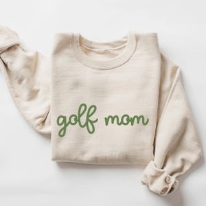 May include: A beige sweatshirt with the text "golf mom" in green cursive lettering.