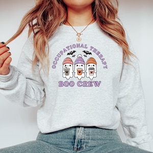 May include: A grey sweatshirt with the text "Occupational Therapy Boo Crew" in purple. Three ghosts wearing hats and holding coffee cups are pictured below the text.